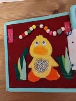 Jucărie de mână din materiale textile și lemn, cu design de pui și elemente de joacă pentru copii.