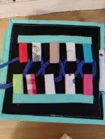 Jucărie educativă pentru copii cu panglici și cordoane de diverse culori și materiale.